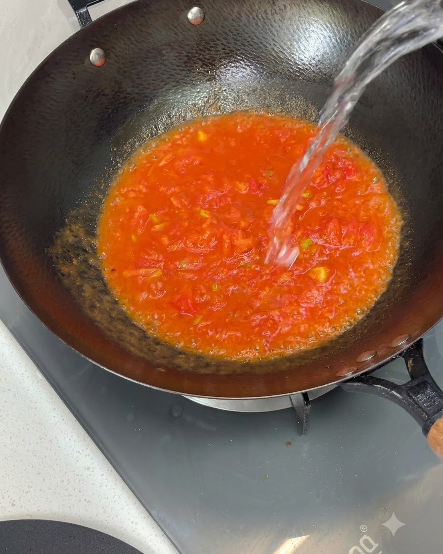 잘 볶아진 토마토 소스가 담긴 웍 위로 물이 위에서 아래로 시원하게 부어지는 모습.