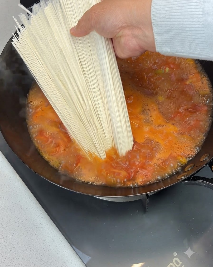 보글보글 끓고 있는 토마토 수프가 담긴 웍 속으로 건면 한 다발이 투입되는 모습.