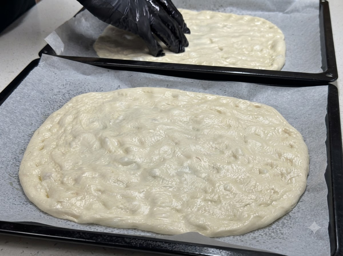 반죽이 펴진 두 개의 베이킹 시트와 표면 전체에 체리 토마토 반 갈라놓은 것을 배치하는 장갑 낀 손.