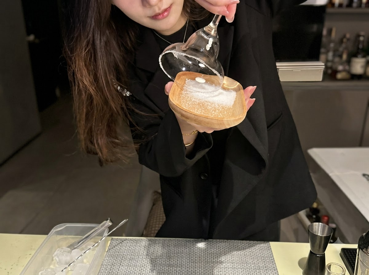 작은 나무 접시에 깔린 바다 소금에 칵테일 잔 가장자리를 찍는 모습