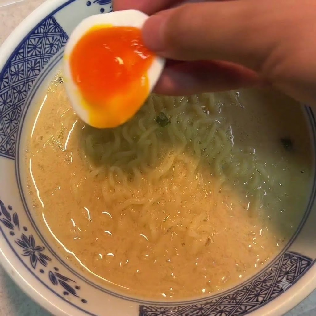 국수 그릇 위로 반숙란 절반을 손으로 들고 있는 모습.