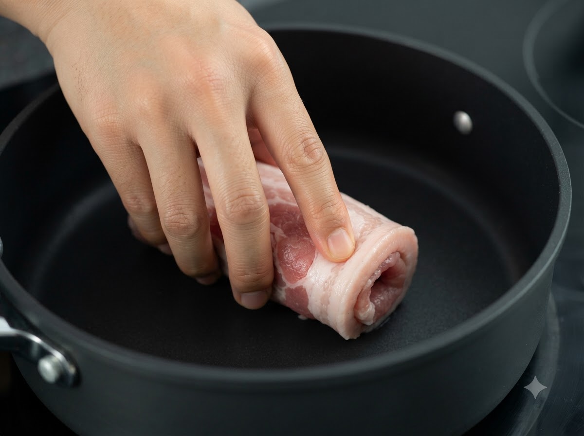 불 위에 올려진 어두운 팬에서 굽고 있는 묶인 삼겹살 롤.