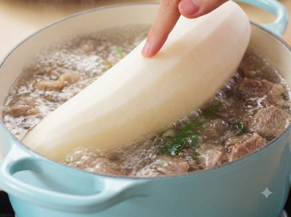 껍질을 벗긴 큰 통무를 끓고 있는 소고기 국물 냄비에 조심스럽게 넣는 손.