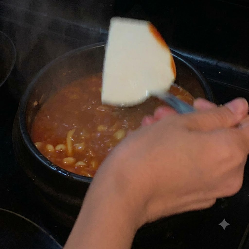 붉은 국물이 끓고 있는 냄비에 뒤집개를 이용해 순두부 한 조각이 내려앉는 모습.