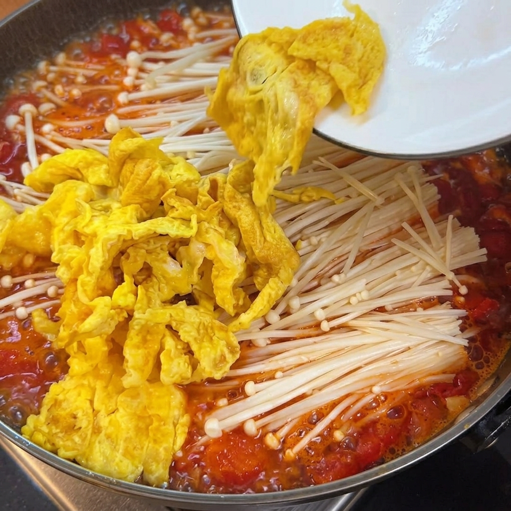 토마토 국물, 버섯, 계란이 담긴 냄비에 추가되고 있는 부드러운 두부 큐브들.