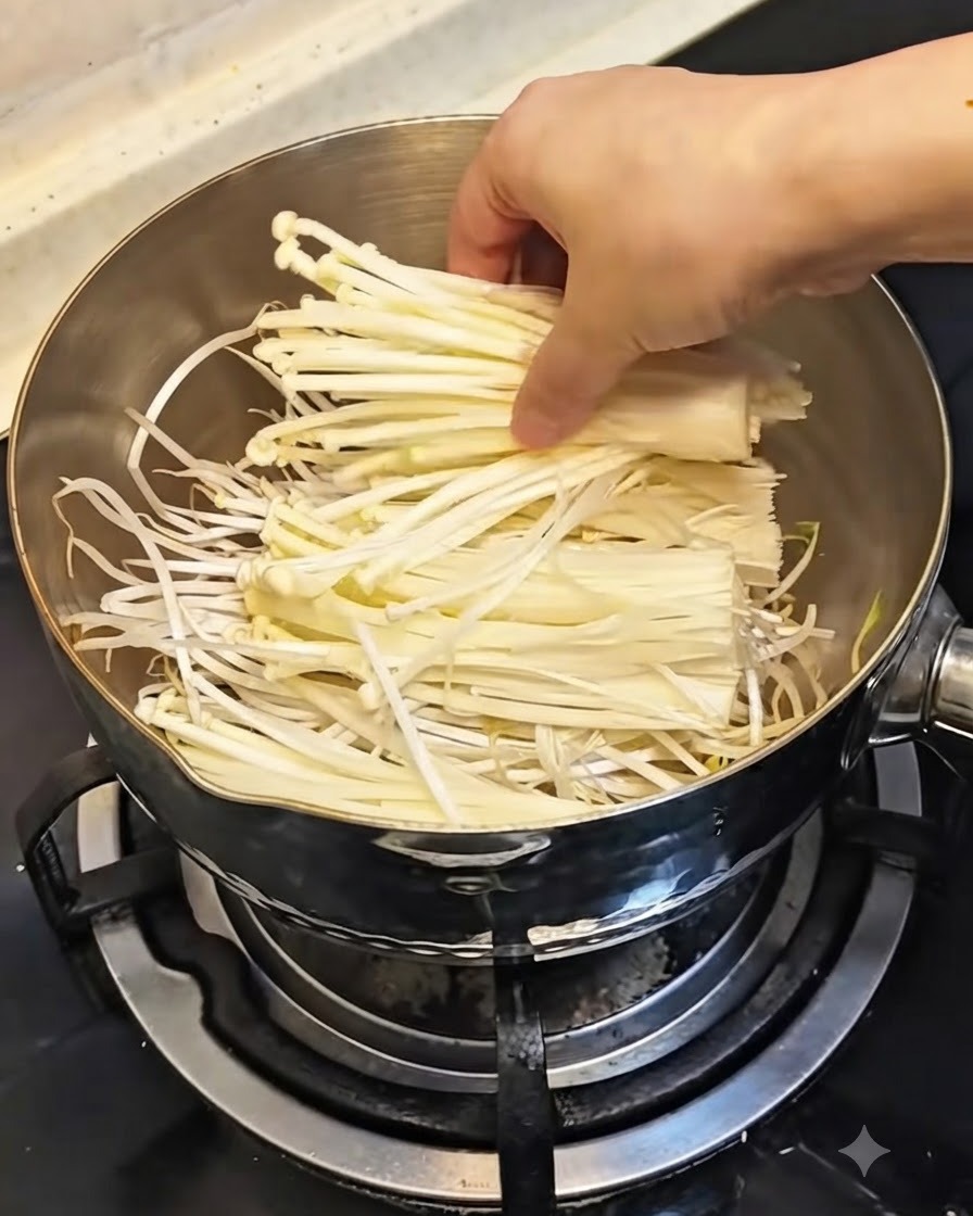 냄비 안의 콩나물 위에 손질된 하얀 팽이버섯 한 묶음을 올리는 모습.