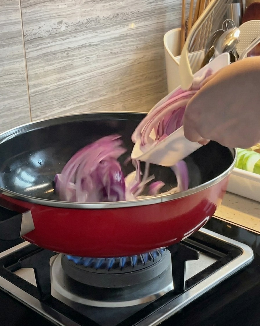 가스 불 위에서 빨간 냄비에 담겨 볶아지고 있는 적양파 슬라이스.