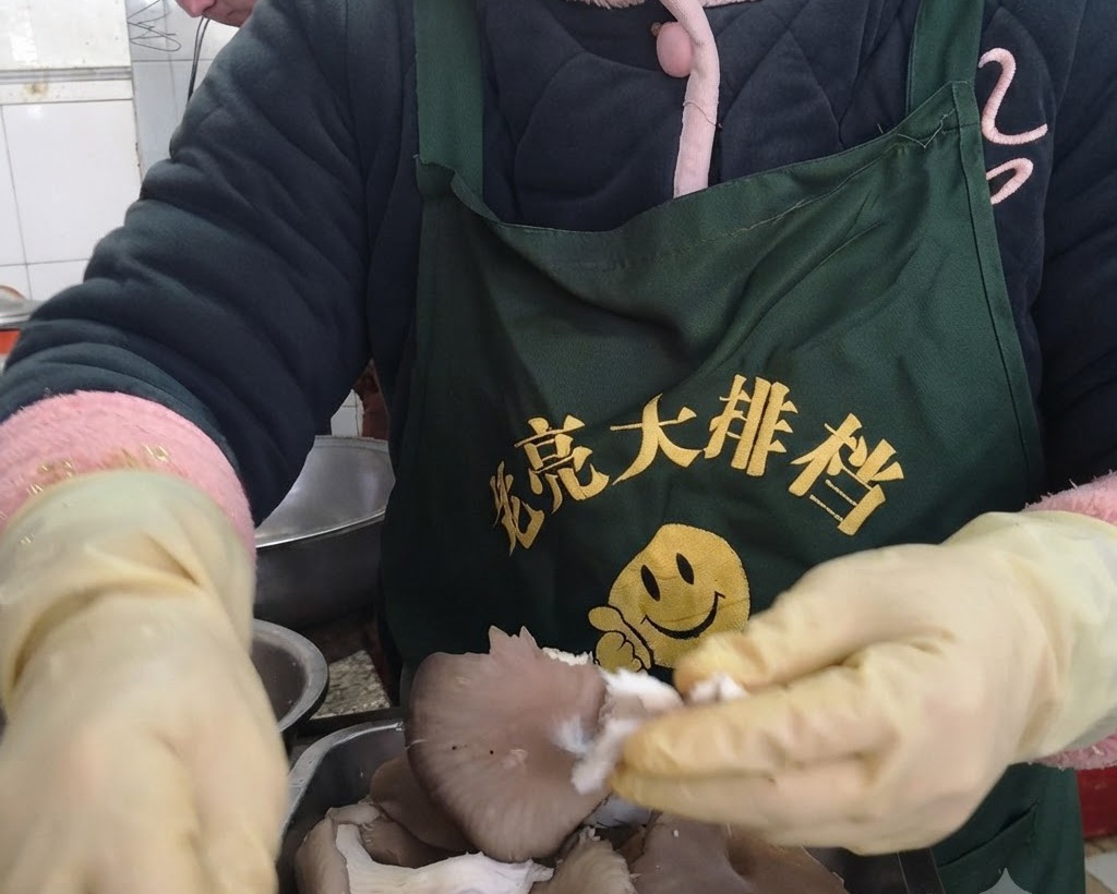 보호용 노란색 장갑을 낀 손으로 신선한 느타리버섯을 한 가닥씩 결대로 찢고 있는 모습.