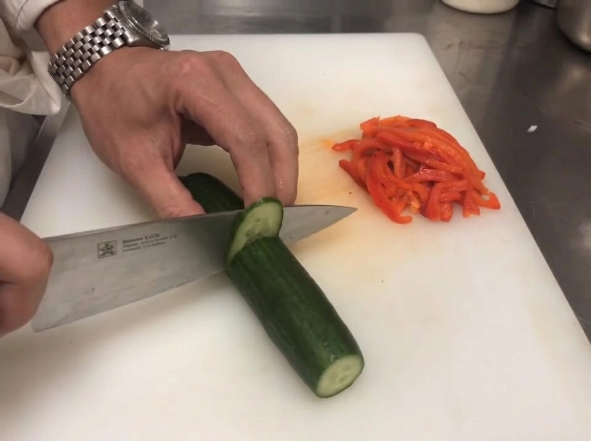 빨간 파프리카 옆에서 신선한 초록색 오이가 칼로 썰리는 모습.