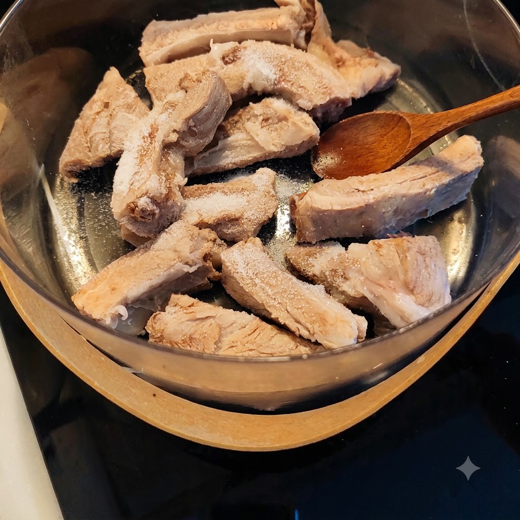소금과 양념이 뿌려진 데친 돼지갈비가 담긴 냄비 위에 나무 숟가락이 놓여 있는 모습.