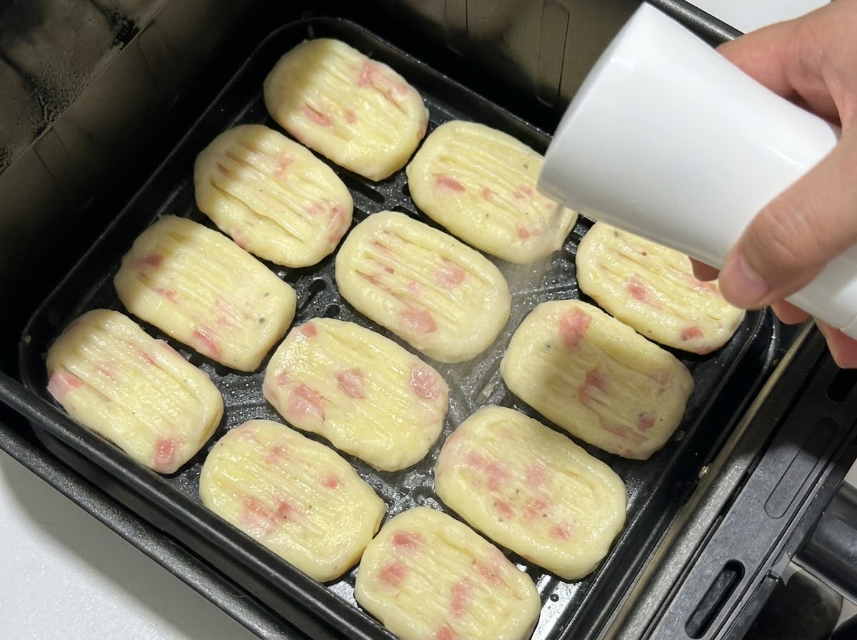 에어프라이어 바스켓에 나란히 담긴 감자 패티에 스프레이 병으로 식용유를 뿌리는 모습.