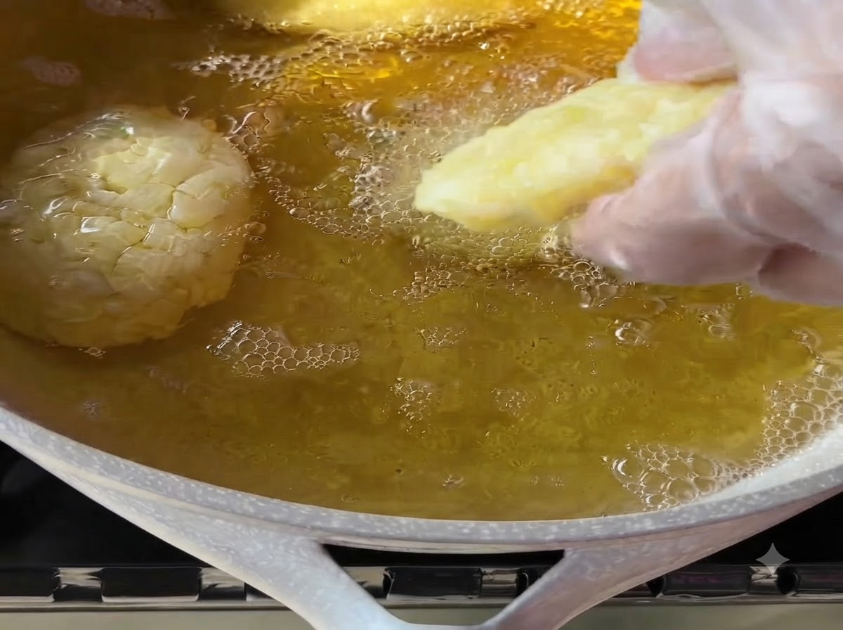 장갑을 낀 손으로 모양을 낸 감자 패티를 거품이 이는 뜨거운 식용유 팬에 조심스럽게 넣는 모습.
