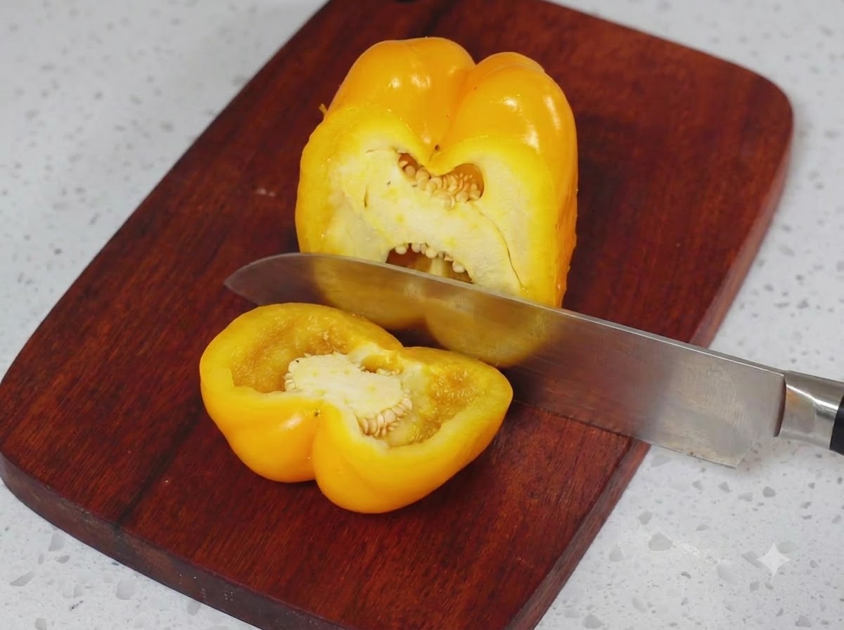 나무 도마 위에서 주방용 칼로 반으로 썰리는 노란색 피망.
