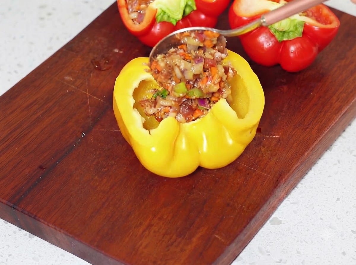 도마 위에서 준비된 고기 소를 숟가락으로 파낸 노란색 피망 반쪽에 채우는 모습.