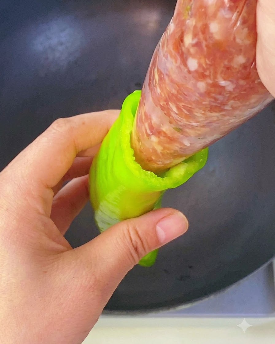 한 손으로 짤주머니에 든 양념된 고기소를 꽈리고추의 빈 속으로 직접 짜 넣고 있는 모습.
