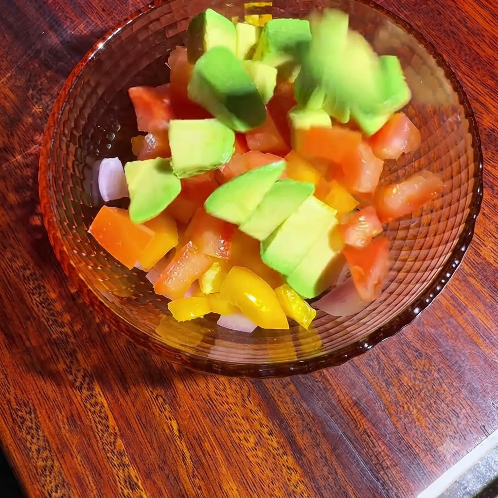 깍둑썰기된 채소와 아보카도가 담긴 그릇에 오일과 레몬즙이 더해져 버무려지고 시즈닝되는 모습.