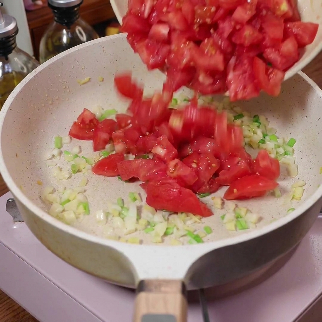 향신 채소가 볶아지고 있는 팬에 깍둑 썬 토마토가 부어지는 모습.