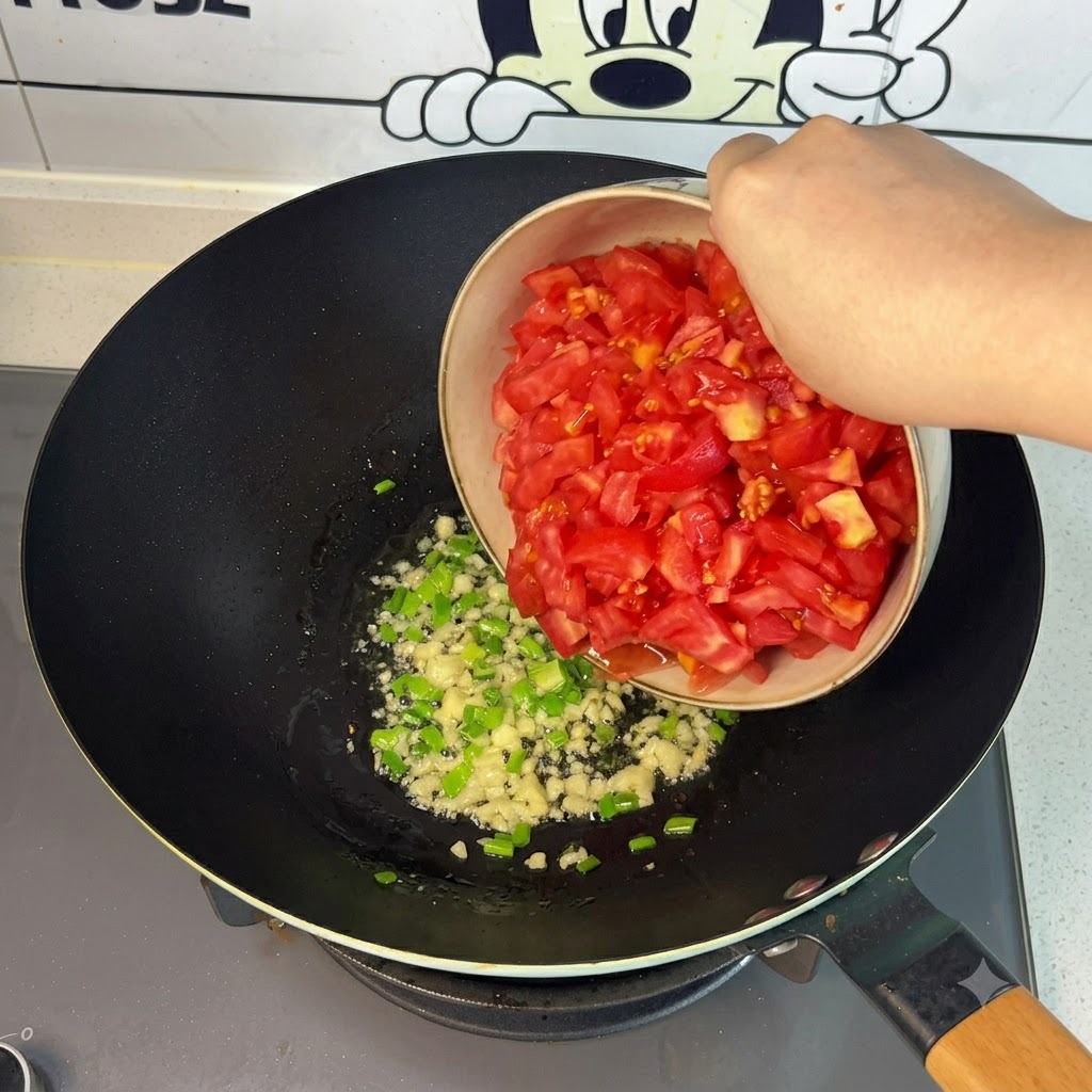 그릇에 담긴 신선하게 썬 빨간 토마토를 웍 안으로 붓는 모습