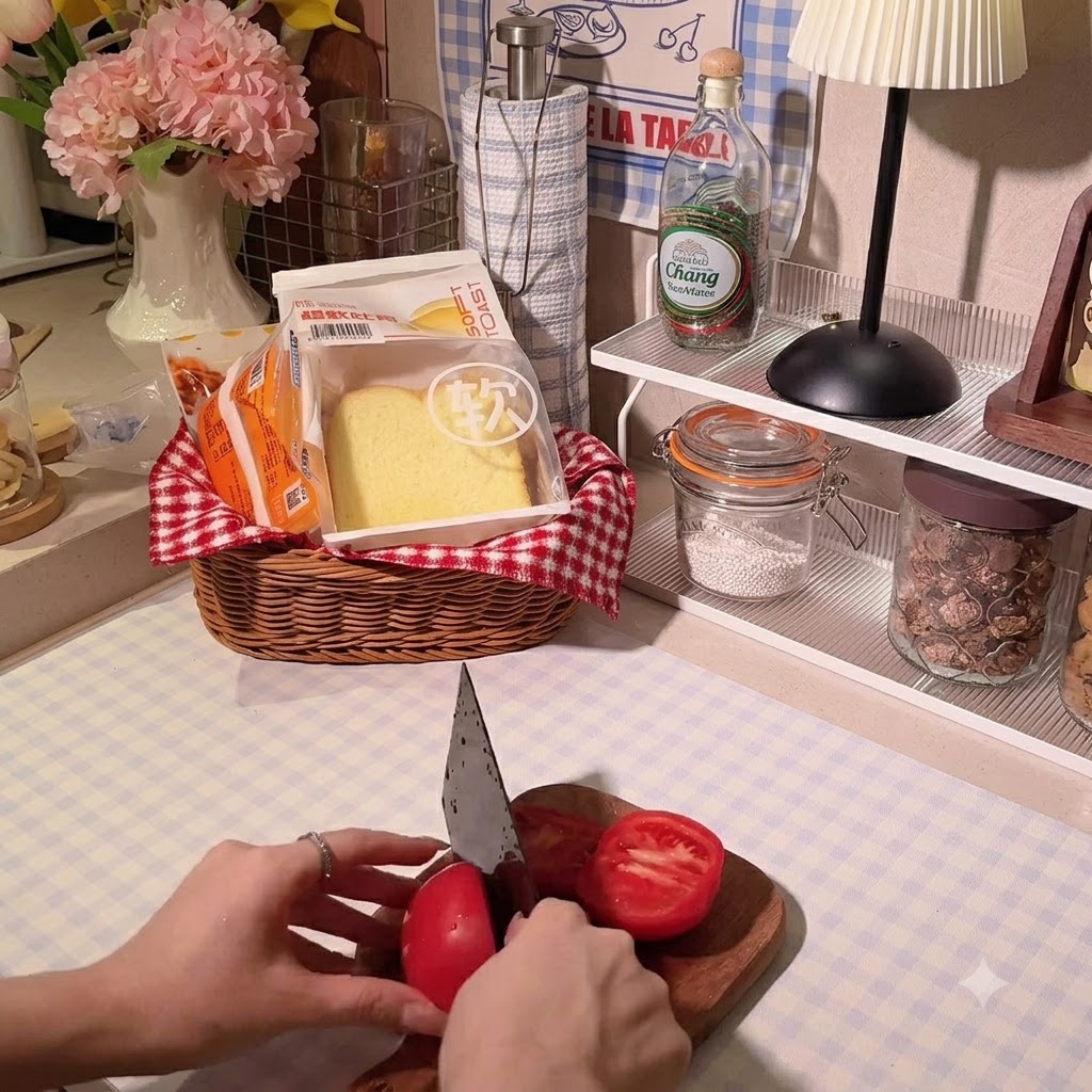 나무 도마 위에서 주방용 칼로 선명한 붉은색 토마토를 썰고 있는 사람의 손.