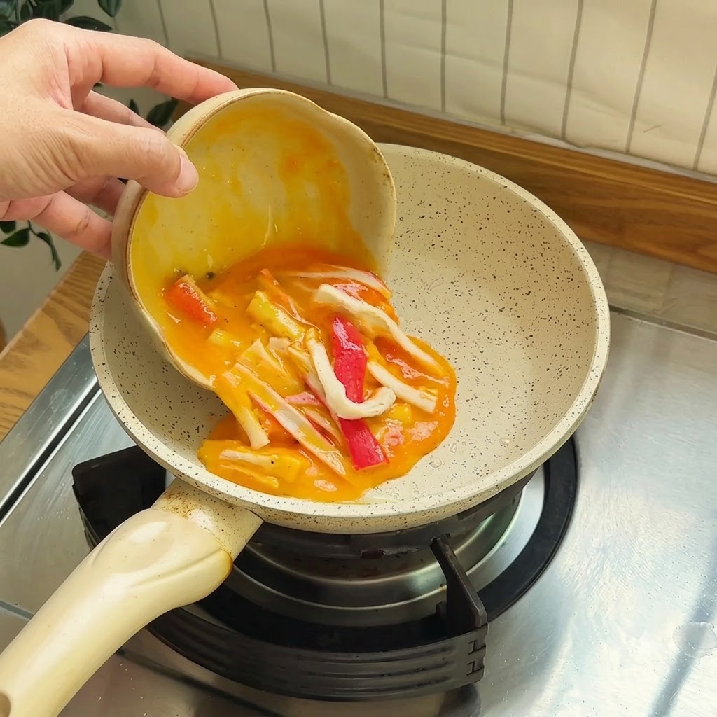 작은 코팅 팬에 게맛살이 섞인 달걀물을 부어 스크램블을 만드는 모습.