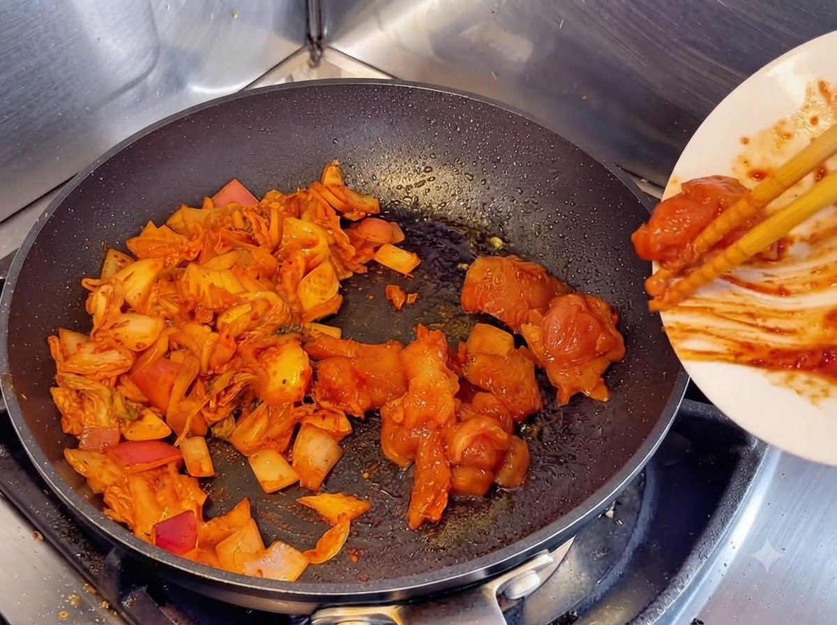 하얀 접시에 담긴 양념된 닭가슴살을 젓가락으로 밀어 넣어 김치와 양파가 볶아지고 있는 팬에 합치는 모습