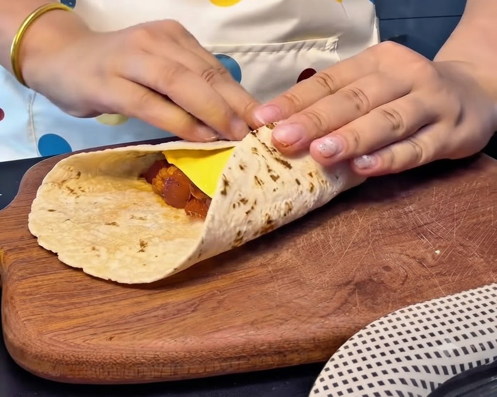 치즈와 속재료를 감싸며 통밀 또띠아의 가장자리를 단단하게 접어 네모난 주머니 모양을 만드는 모습