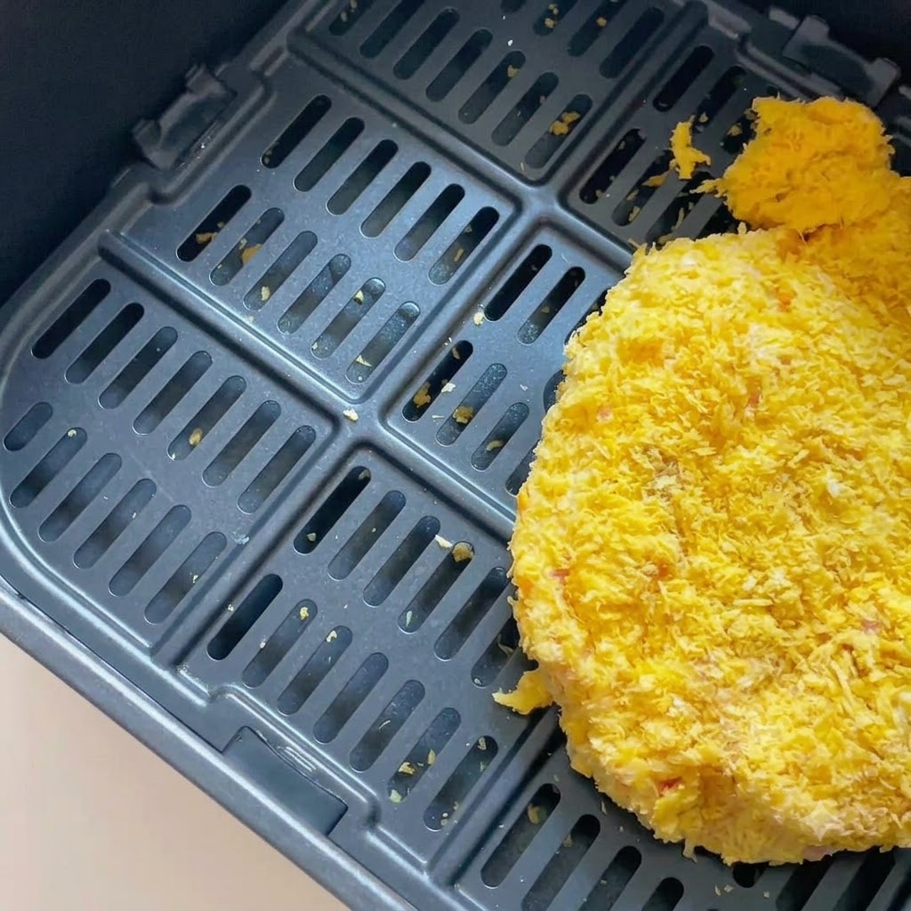 어두운 색상의 에어프라이어 바스켓 안에 들어 있는 빵가루 입힌 돈가스.