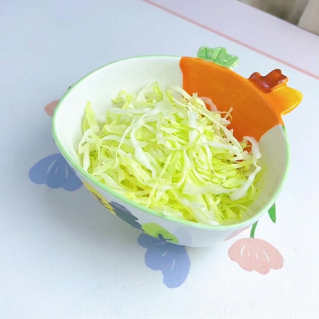 오렌지색 당근 모양 손잡이가 있는 장식용 그릇 안에 곱게 썬 양배추가 깔끔하게 담겨 있는 모습.