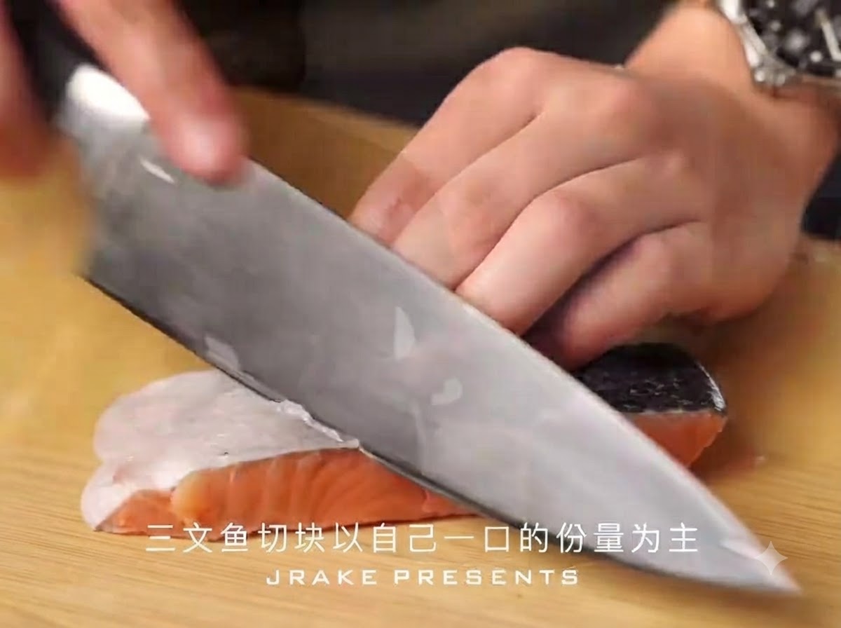 나무 도마 위에서 날카로운 셰프 나이프가 껍질이 붙은 연어 필렛을 한 입 크기로 썰고 있는 모습.