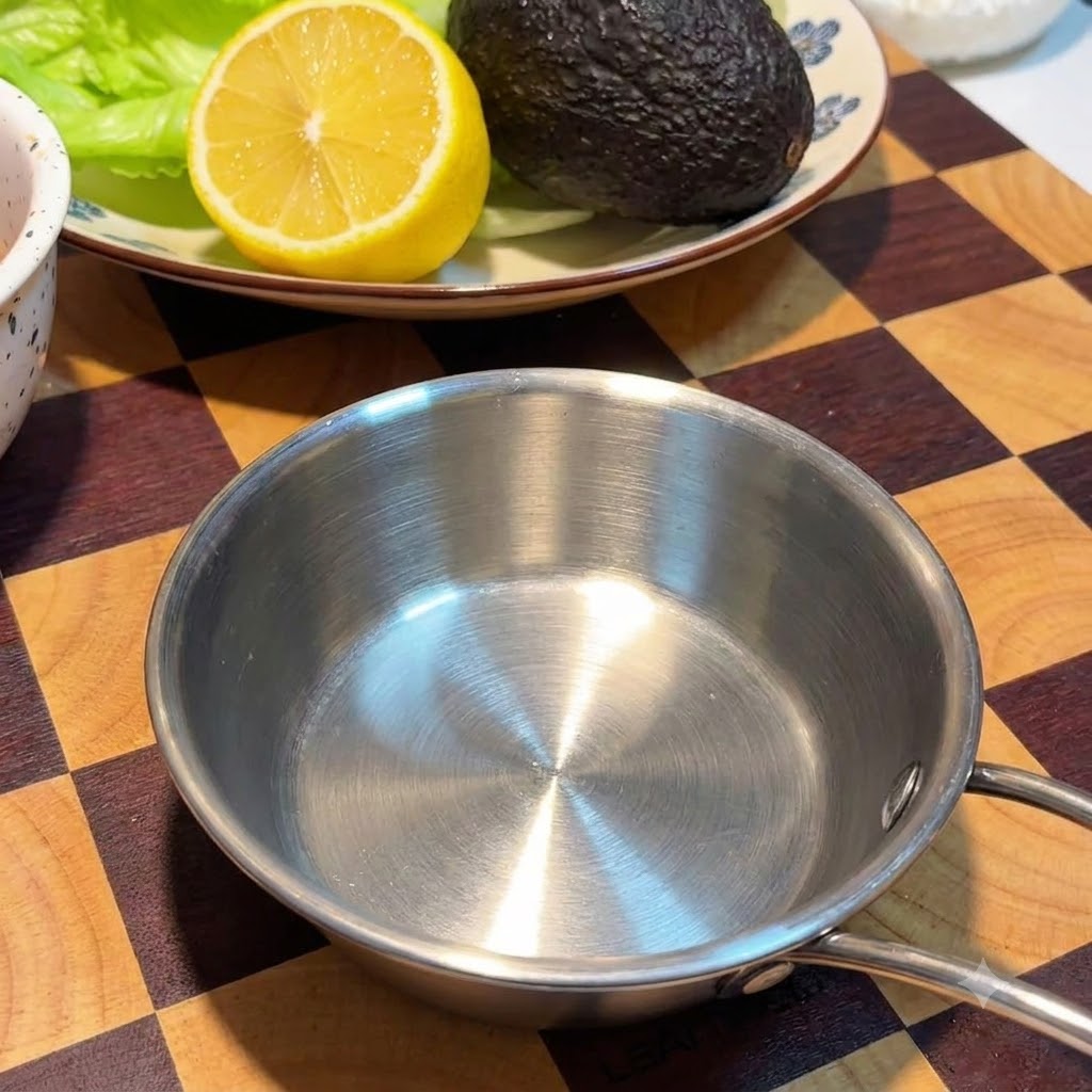 격자무늬 나무 도마 위, 레몬과 아보카도가 놓인 접시 옆에 놓인 빈 스테인리스 그릇.