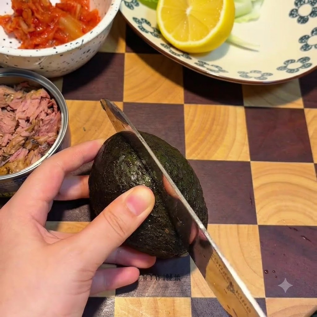 나무 도마 위에서 칼로 아보카도를 씨를 따라 반으로 가르는 모습.