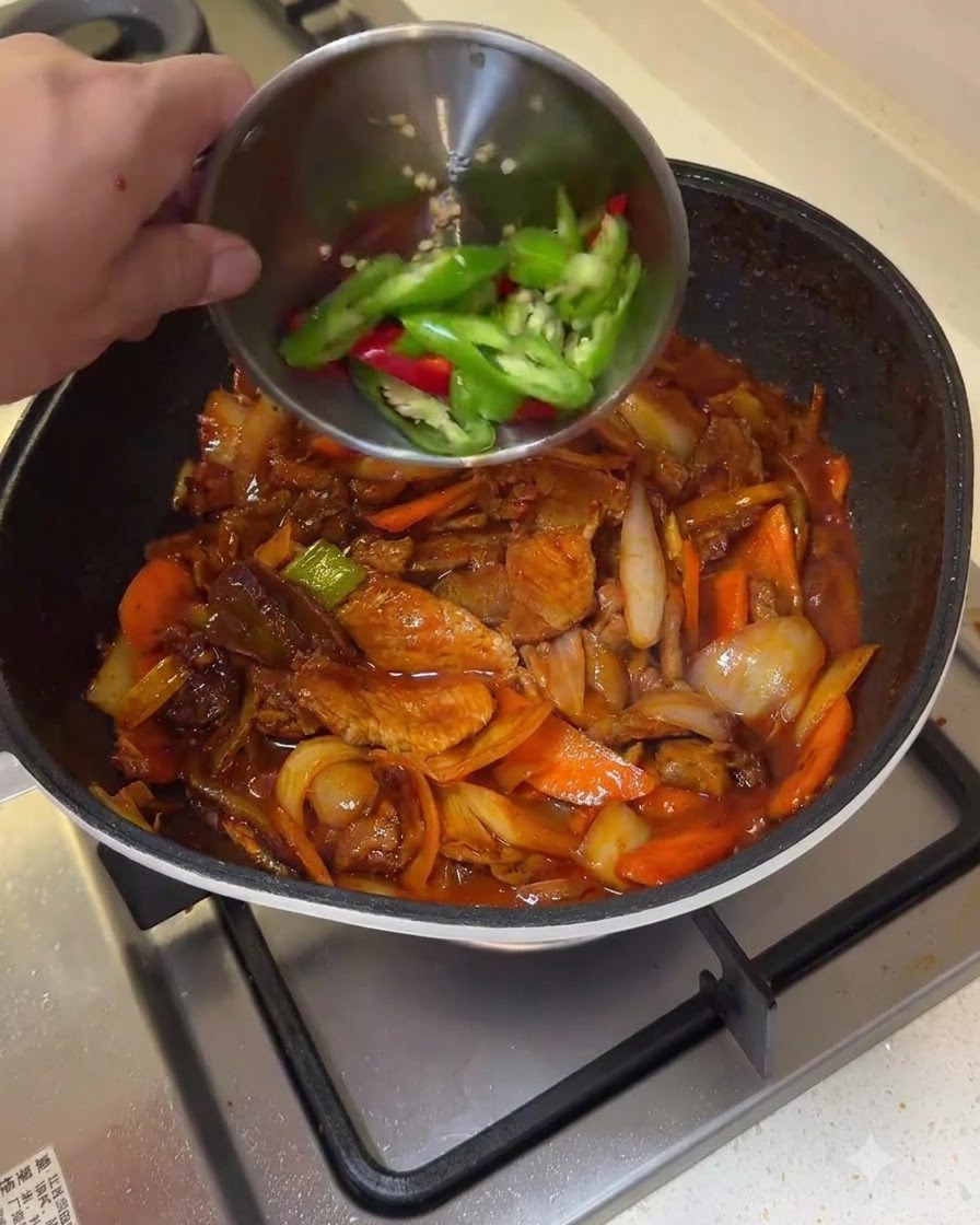 작은 그릇에 담긴 청홍고추 슬라이스를 볶아진 제육볶음 팬에 붓는 모습