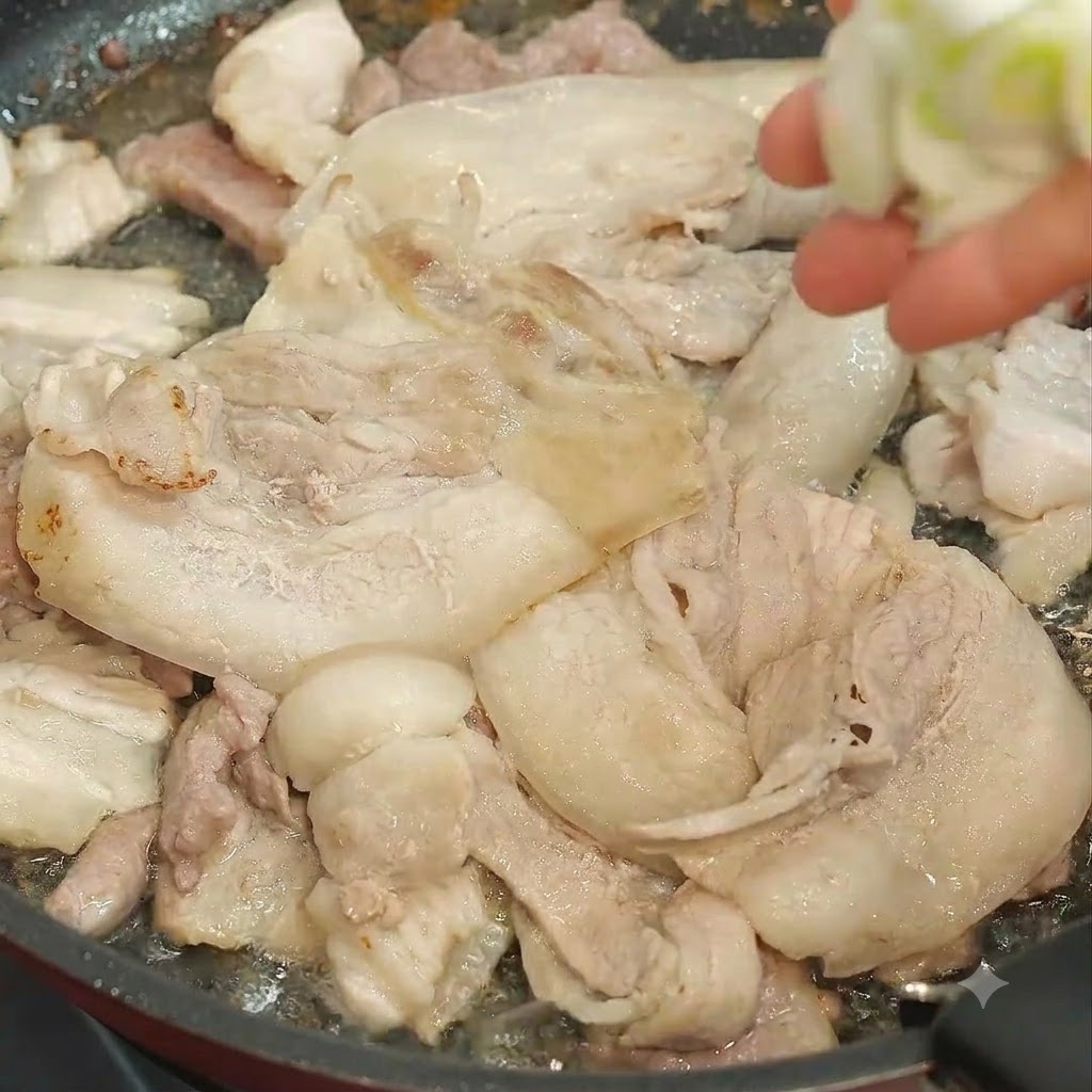 고기가 볶아지고 있는 팬에 썰어둔 대파를 손으로 넣고 있는 모습.