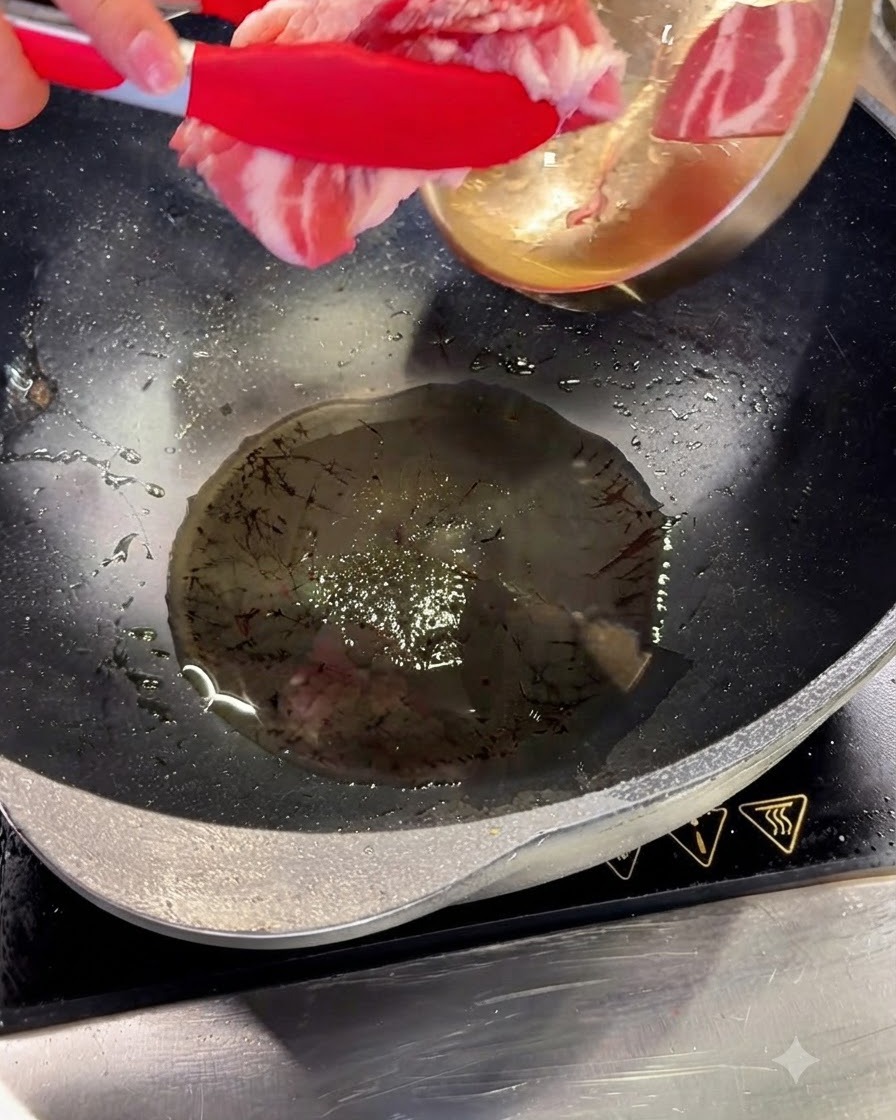 빨간 집게를 사용하여 달궈진 기름에 삼겹살 슬라이스를 넣고 있는 웍의 모습