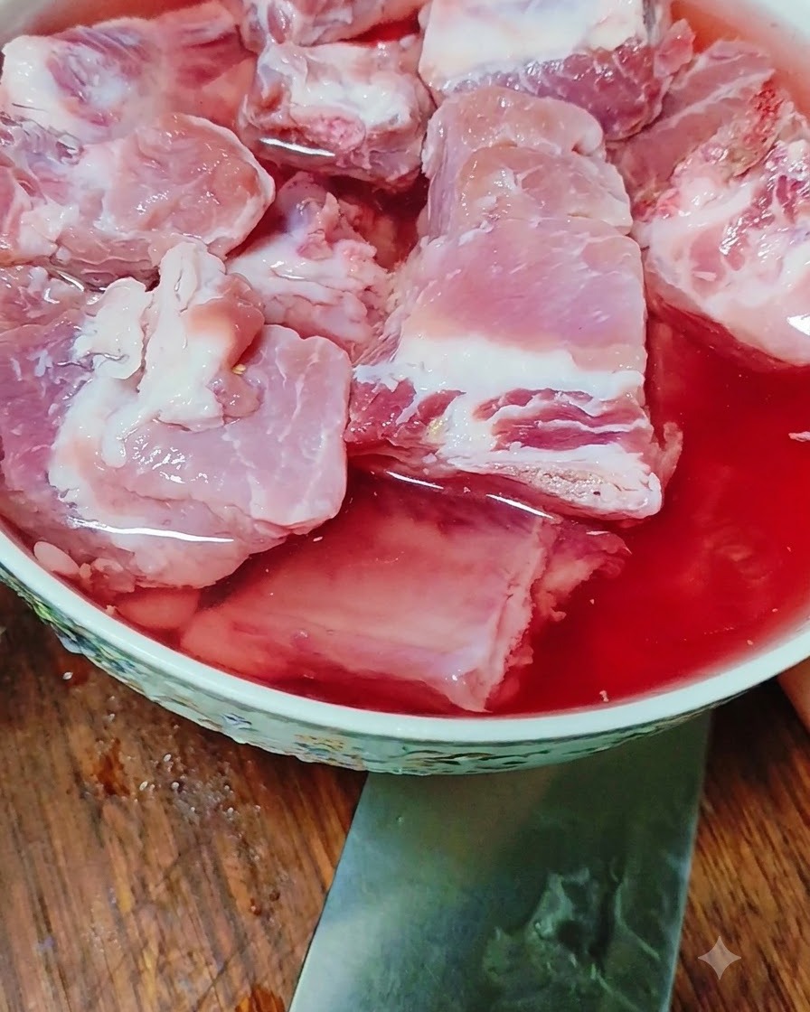 붉은빛 물이 담긴 그릇에 생돼지고기 갈비가 담겨 물에 잠겨 있는 모습.