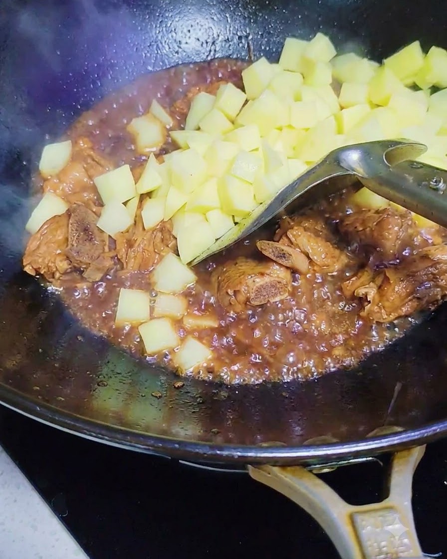 양념된 돼지고기 갈비와 소스가 담긴 웍에 깍둑 썬 생감자를 넣는 모습.