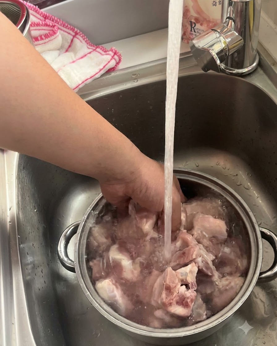 주방 수도꼭지 아래 금속 볼에서 물에 담겨 씻기고 있는 돼지고기 갈비.