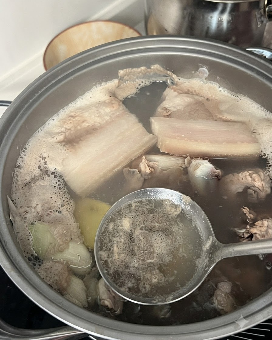 돼지고기 갈비가 들어있는 냄비의 끓는 물에서 거품과 불순물을 구멍 조리개로 건져내는 모습.