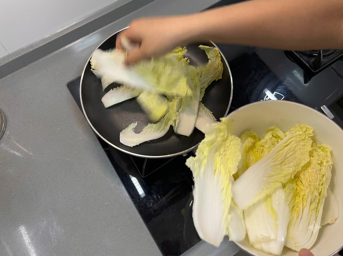 프라이팬 바닥에 알배기 배추 잎을 깔아 보호 층을 만드는 모습.