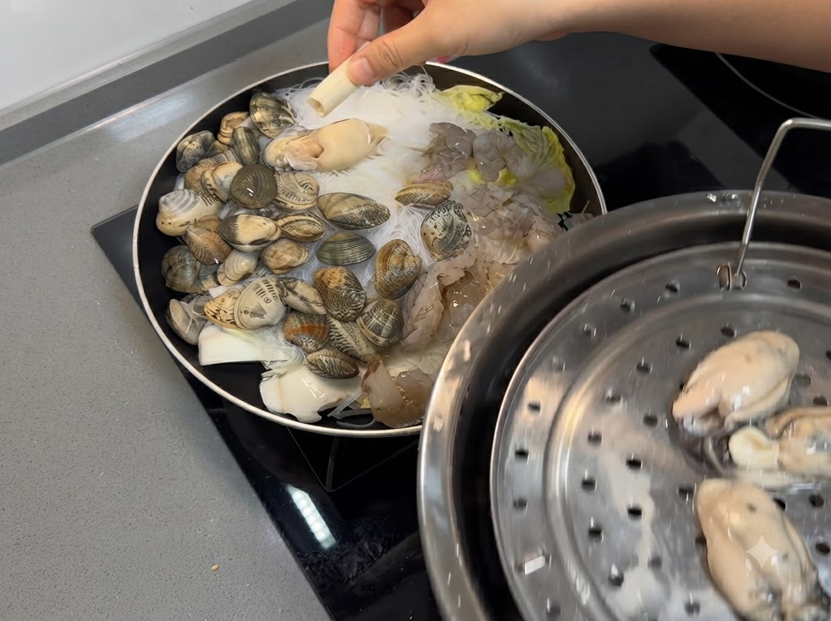 팬 안의 해산물과 당면 혼합물 위에 새우와 신선한 굴을 올려놓는 모습.