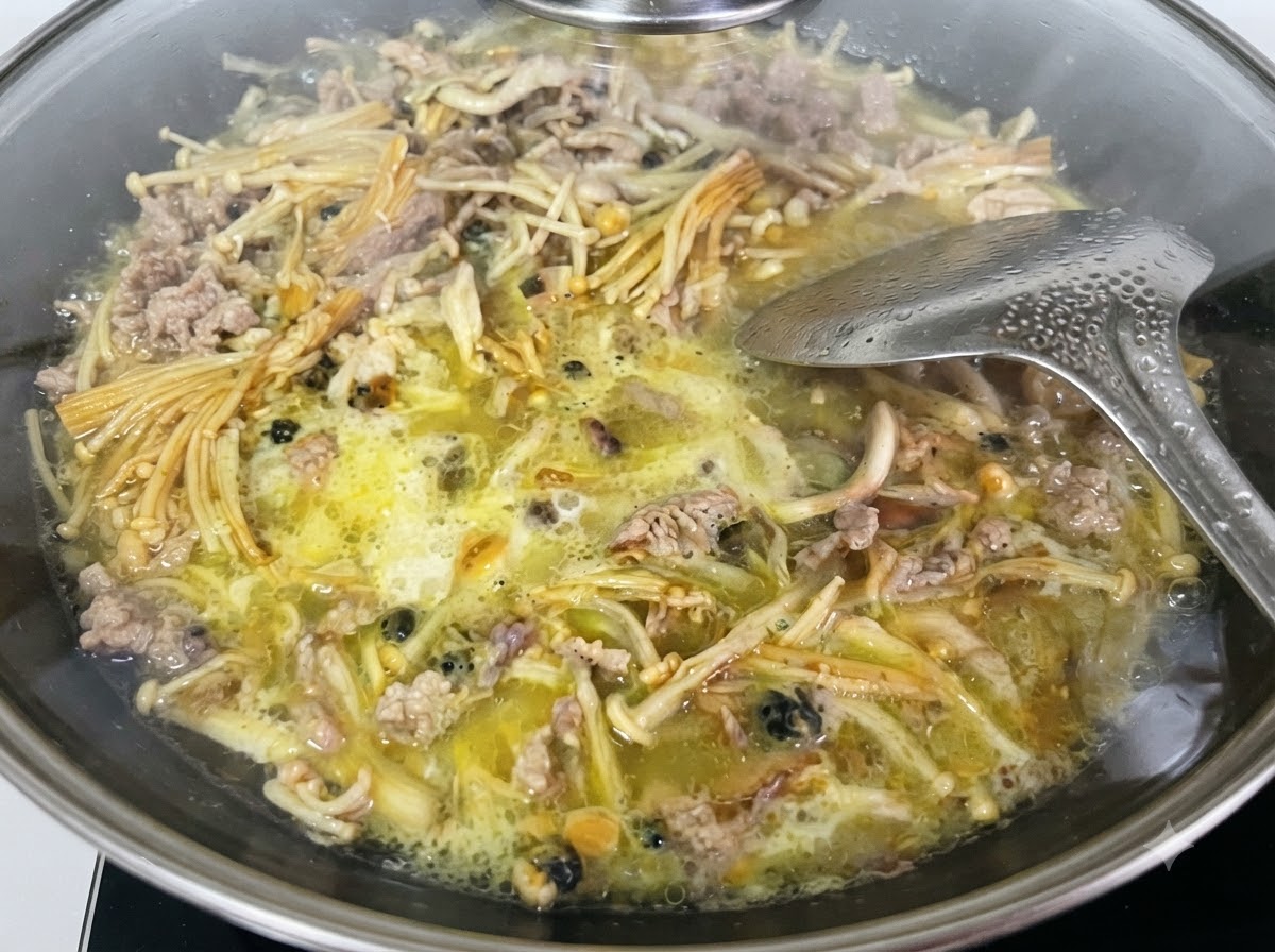 계량컵에 담긴 액체 상태의 고구마 전분물을 웍 안으로 붓고 있습니다.