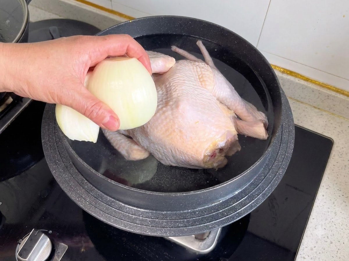 통닭과 물이 담긴 냄비에 반으로 썬 양파와 향신채를 넣는 모습