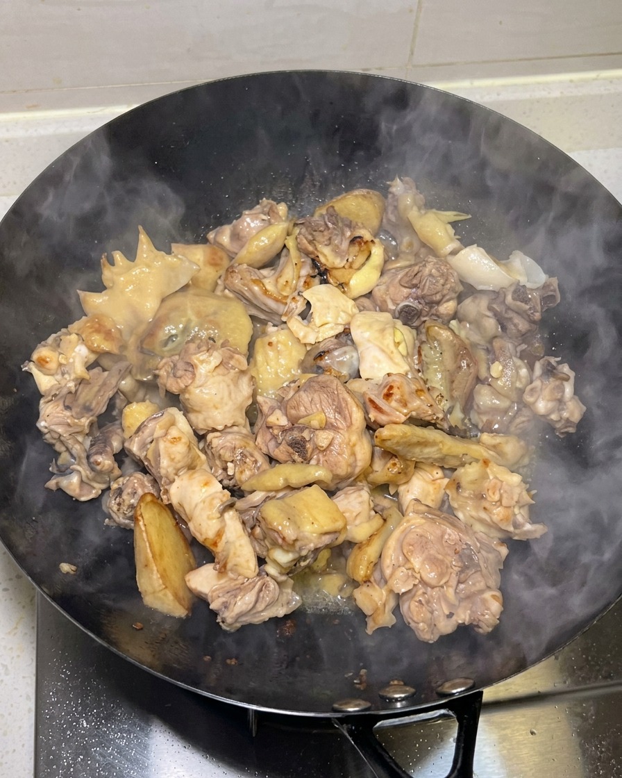웍에서 노릇하게 구워진 닭고기 위로 연기가 피어오르는 모습.