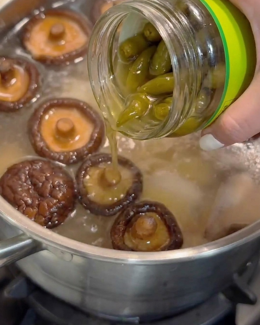 유리병에서 표고버섯이 담긴 끓는 수프 냄비로 절인 껍질 벗긴 고추 국물을 붓는 모습.