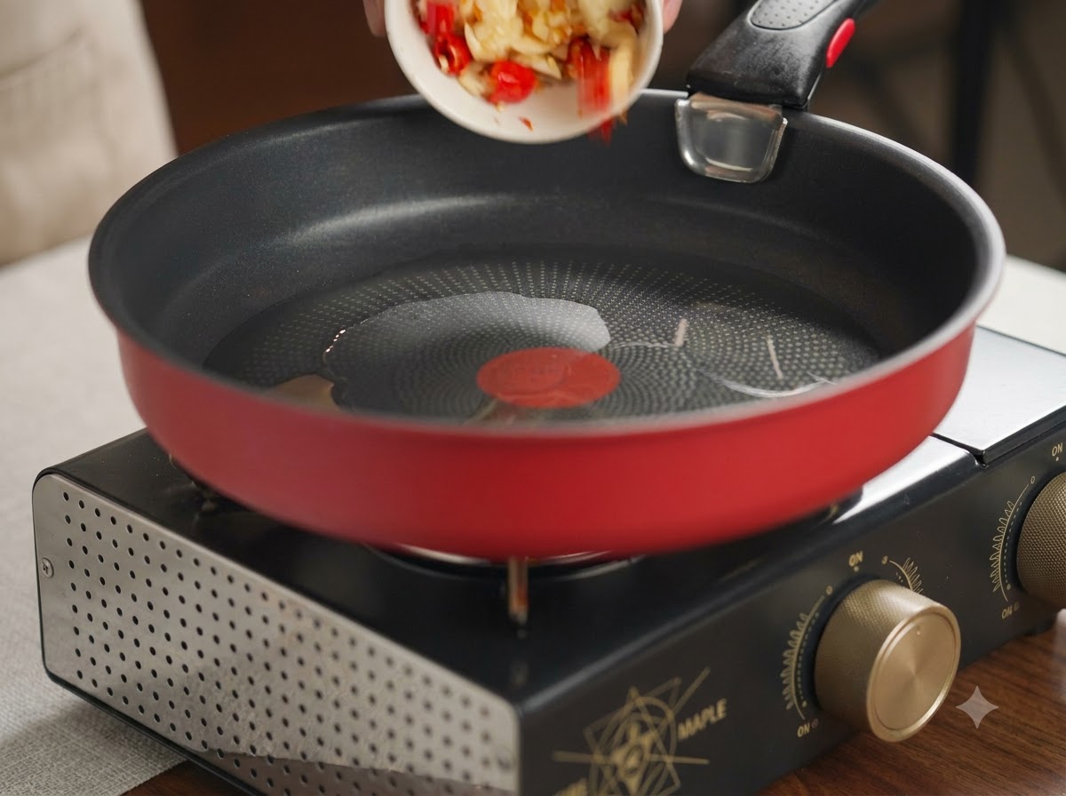 Crushed garlic and red chilies being tipped from a small white dish into a hot red frying pan with oil.