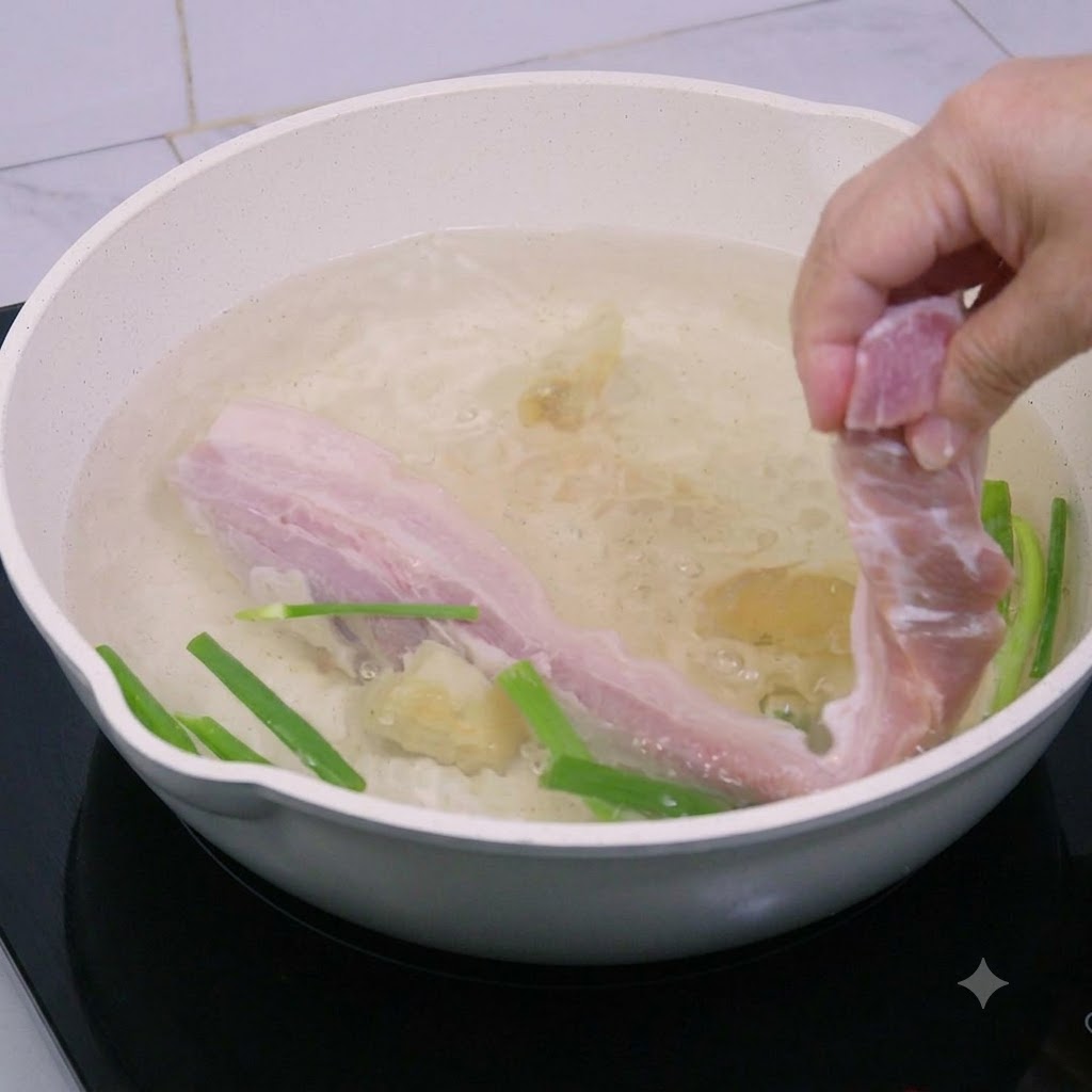 생강과 쪽파가 들어간 끓는 물 냄비에 삼겹살 줄기를 넣는 모습.