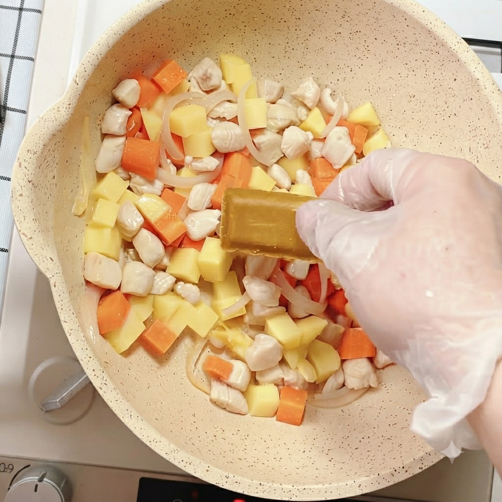 채소와 닭고기가 든 팬에 카레 블록을 올리는 손