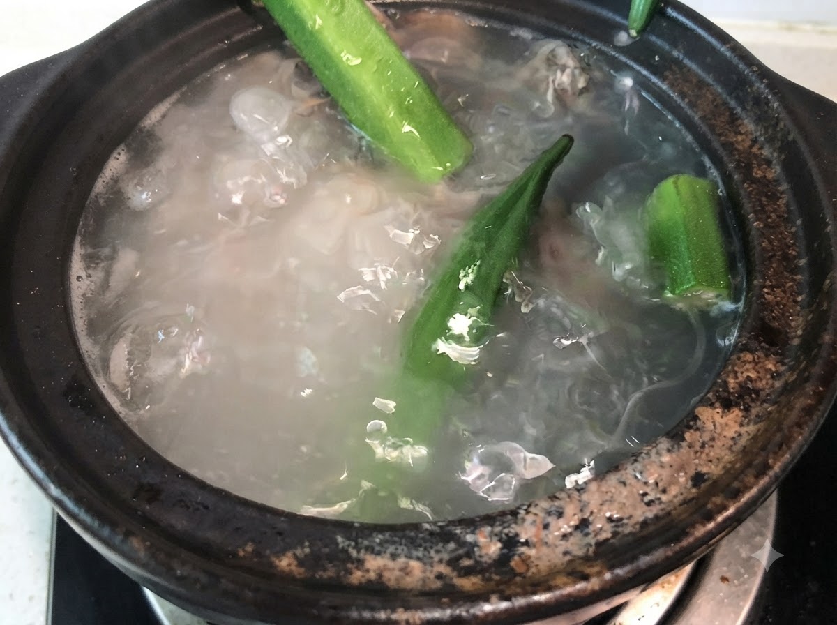 끓고 있는 돼지등뼈 육수에 통째로 손질된 초록색 오크라 꼬투리를 넣는 모습.