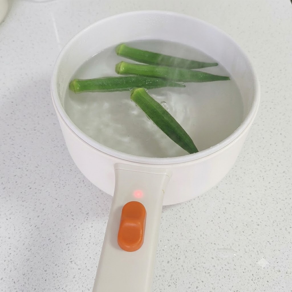 젓가락으로 끓는 물에서 조리된 초록색 오크라를 들어 올리는 모습.