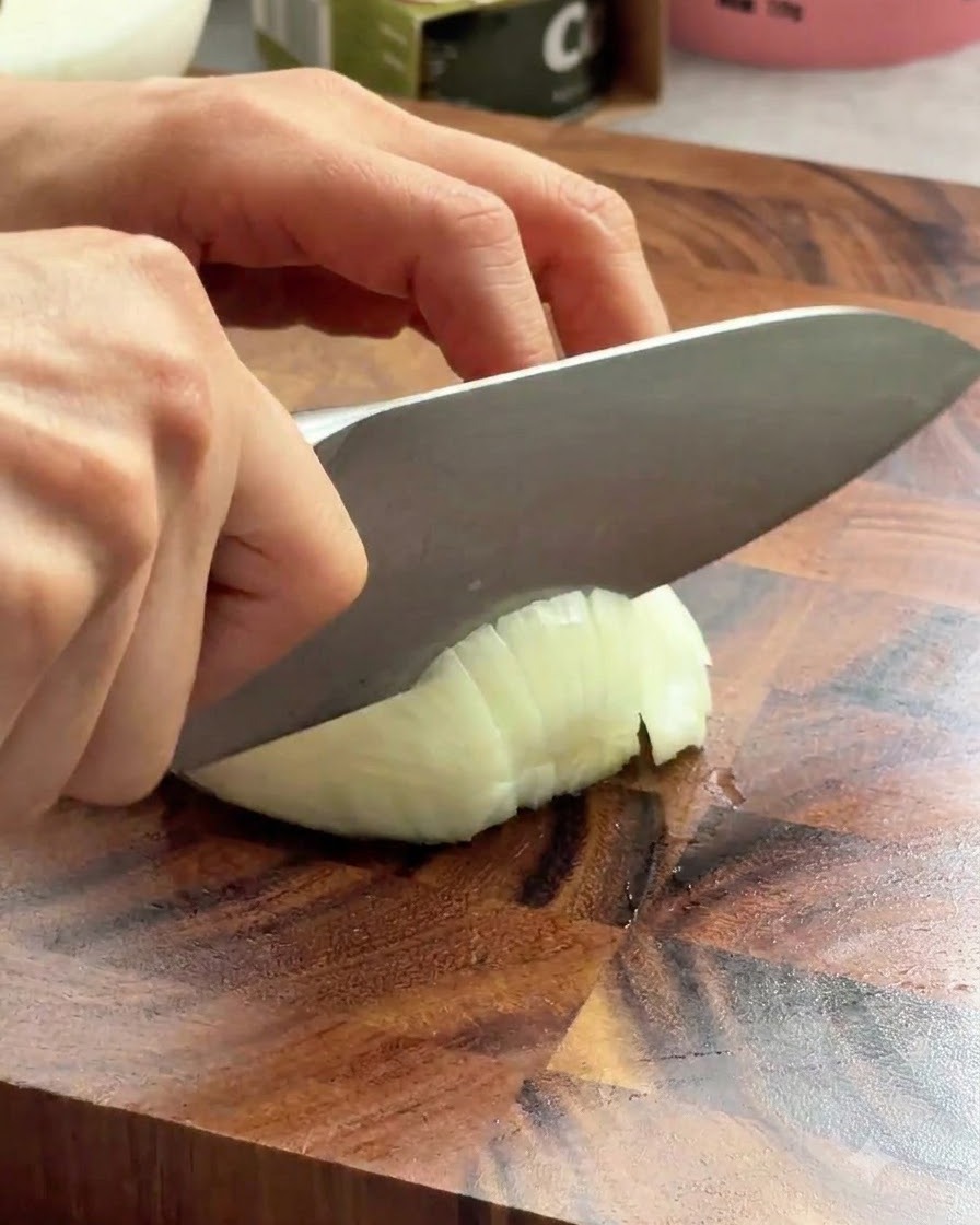 나무 도마 위에서 날카로운 요리용 칼로 흰 양파를 썰고 있는 모습